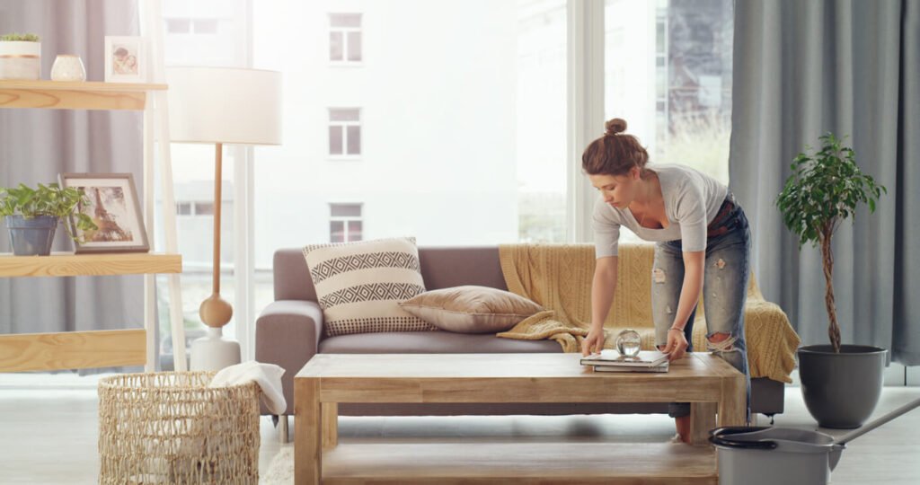 Woman tidying a bright living room with a sofa and coffee table